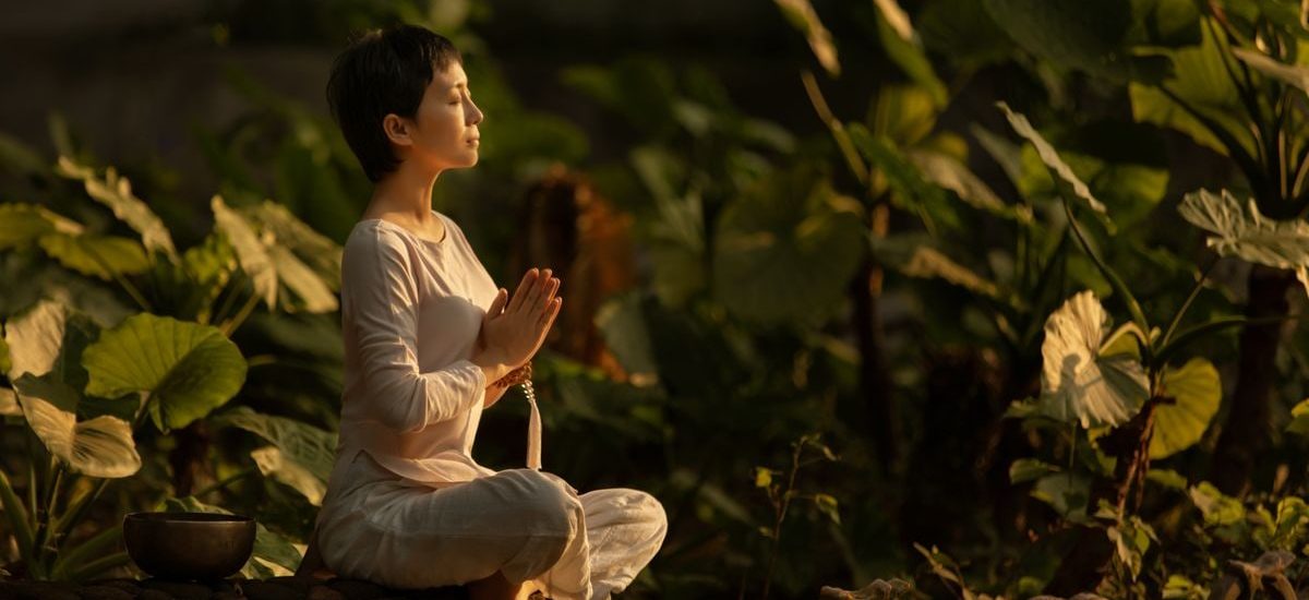 Serene scene of a woman meditating in a lush garden setting at daylight.