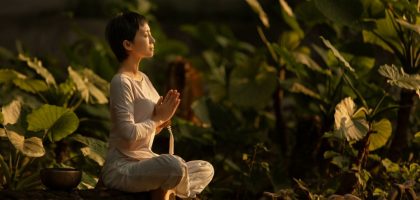 Serene scene of a woman meditating in a lush garden setting at daylight.