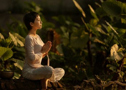 Serene scene of a woman meditating in a lush garden setting at daylight.