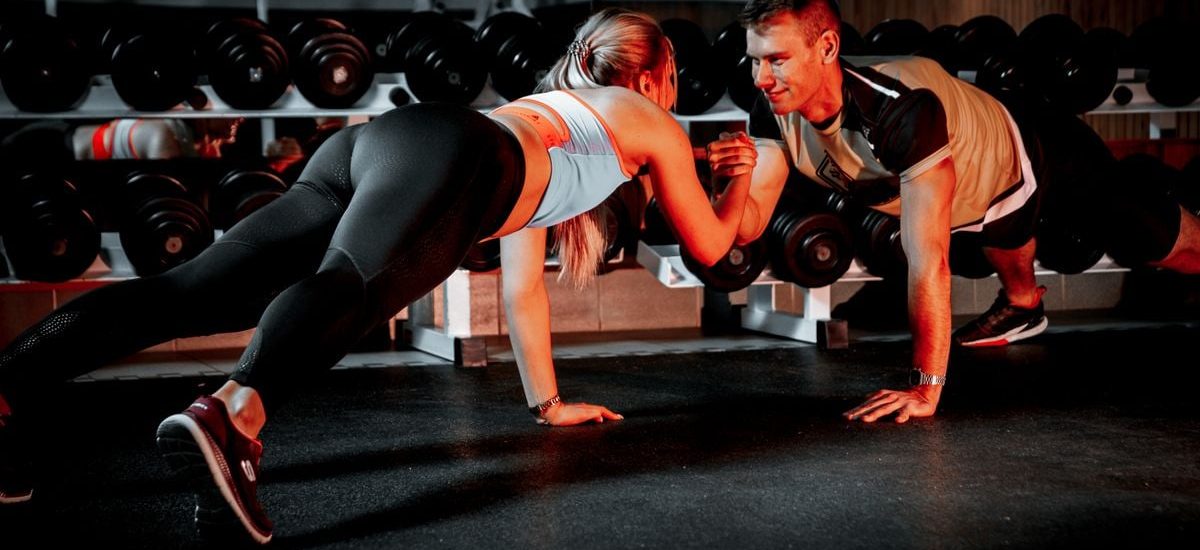 A couple collaborates in a partnered push-up workout session at the gym, symbolizing fitness and teamwork.
